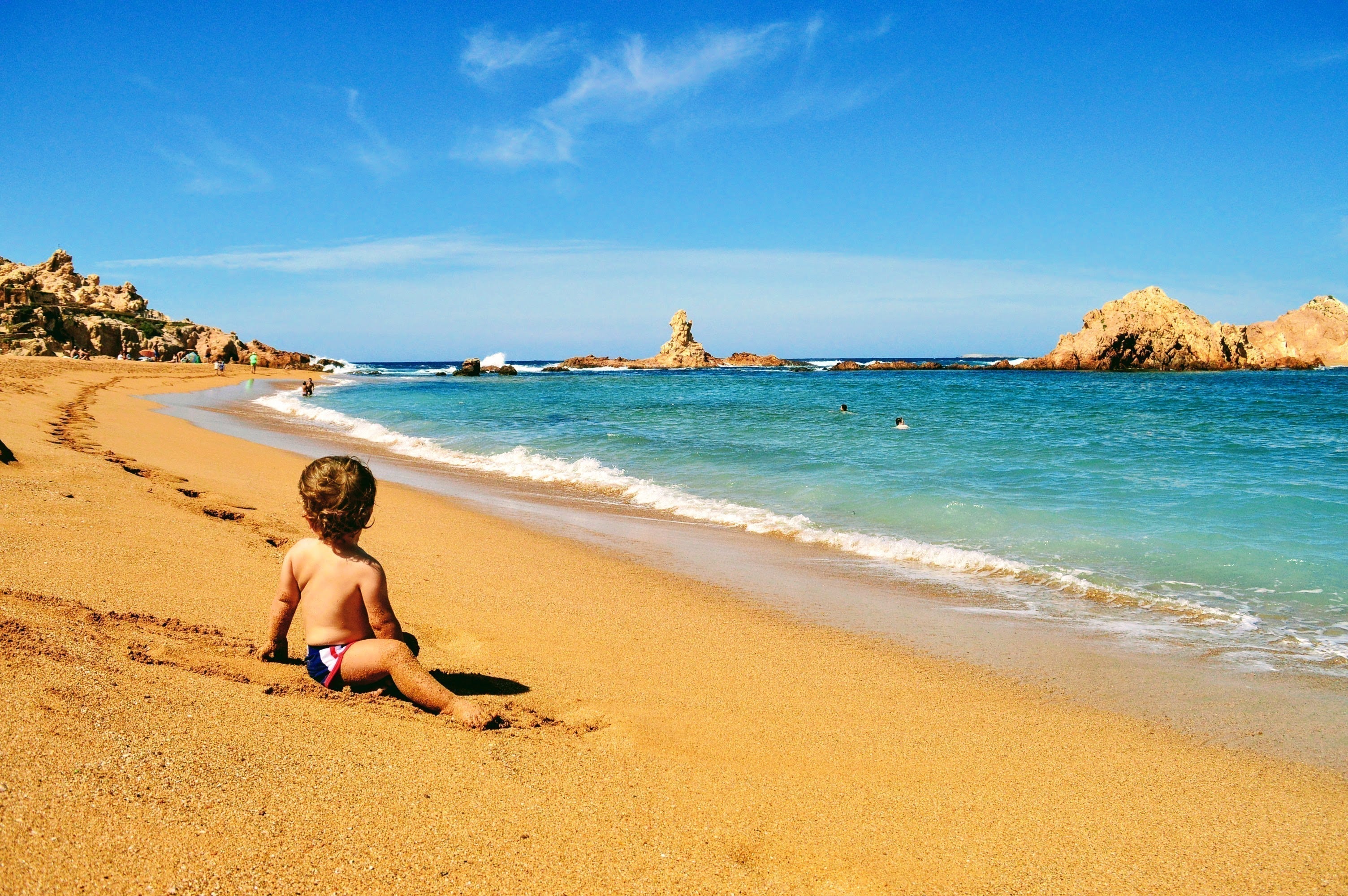 A boy looking down the golden sand beach of Pregonda, on the north coast of Menorca.