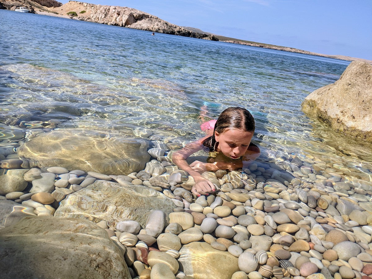 A girl looking at rocks through the crystal clear waters of Menorca, a Biosphere Reserve.