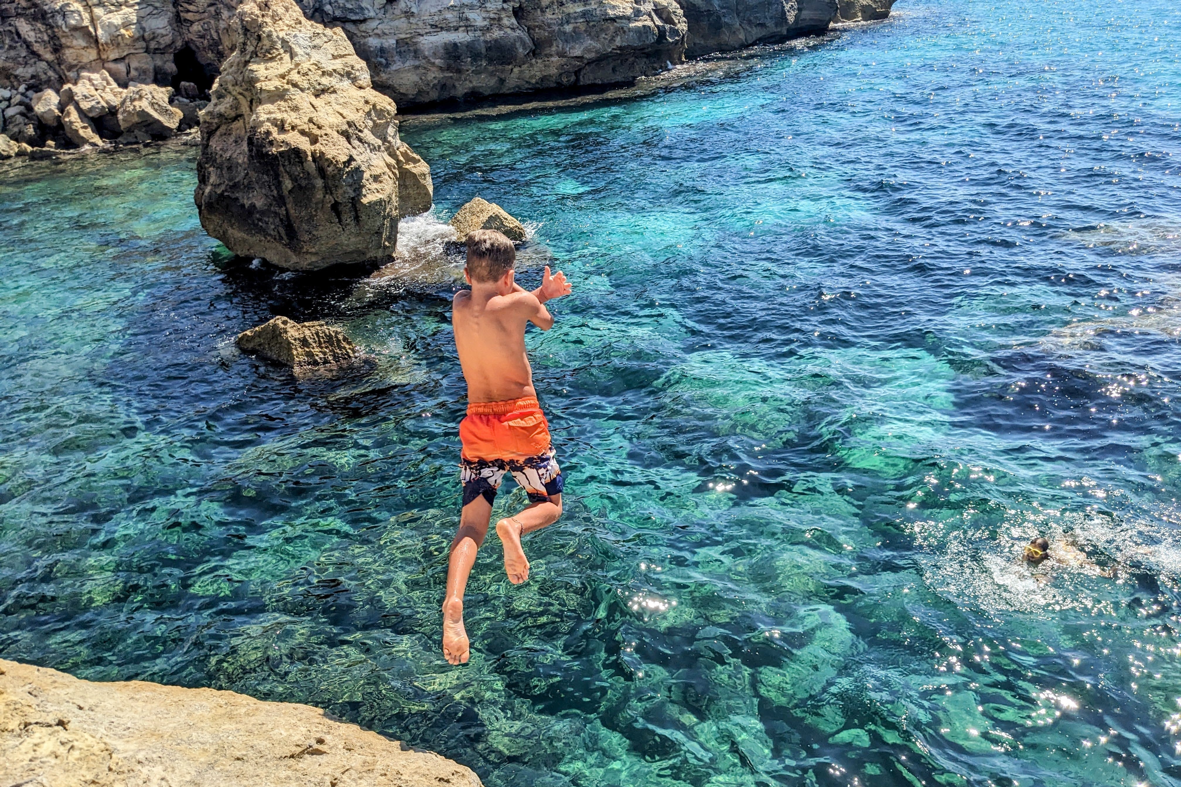A boy jumping off the rocks into the crystal clear waters of Menorca.