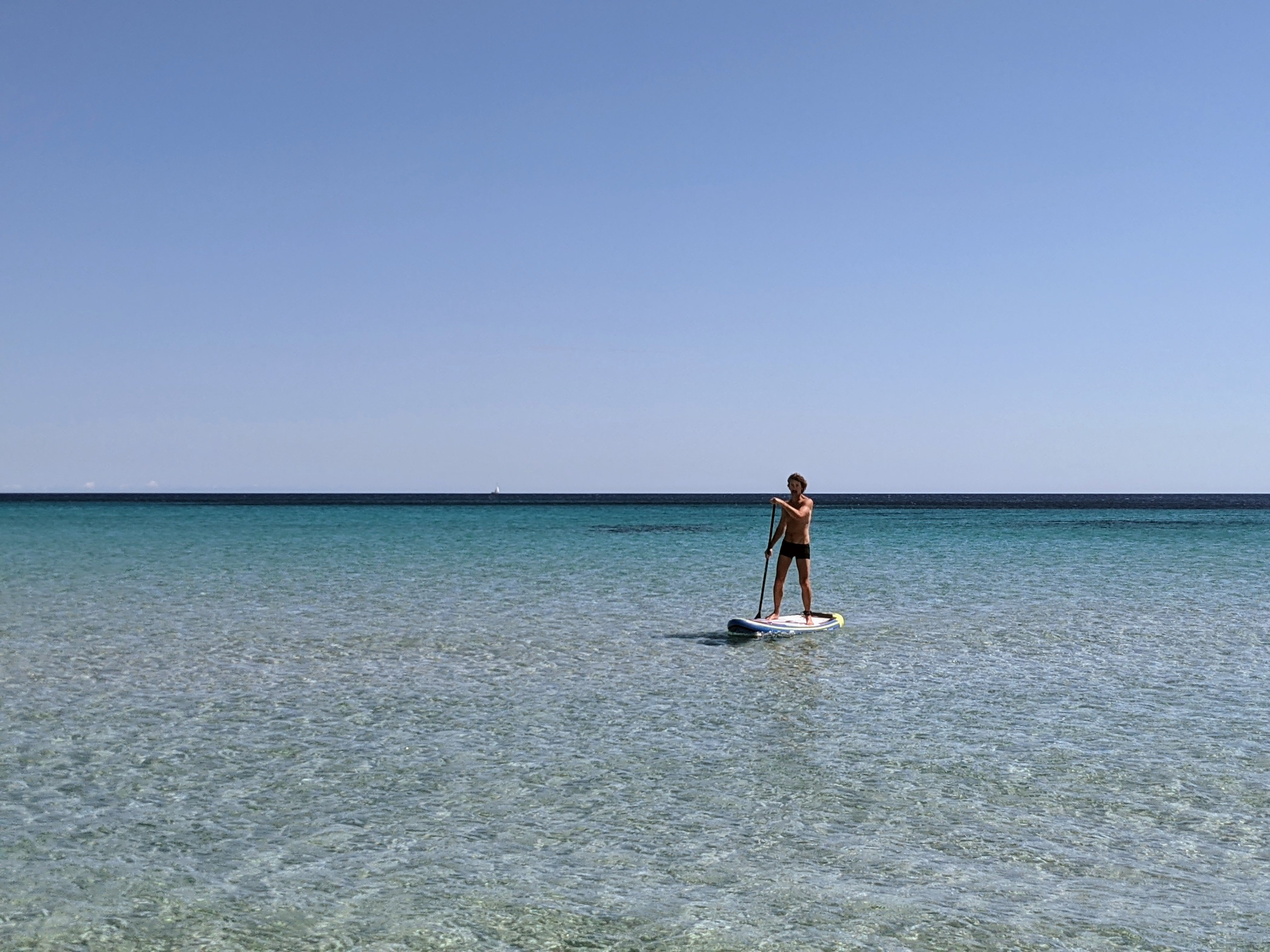 A man paddle boarding on the calm, clear, blue waters of the Balearic Sea, a great thing to do in Menorca.